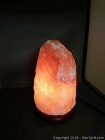 Lit Himalayan salt lamp glowing orange on wooden base against dark background.
