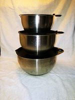 Stacked set of three stainless steel mixing bowls showing polished surfaces and handles