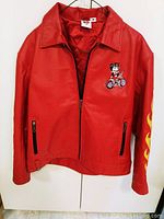 Full front view of the red leather jacket hanging, showing embroidered Betty Boop motorcycle design and zipper pockets.