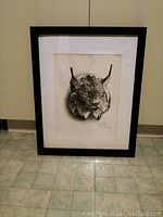 Full front view of framed lynx drawing leaning against wall on tiled floor