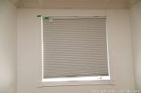 White cellular window shade fully extended inside window frame with some dented pleats, showing mounting hardware.