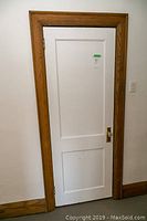 Full view of a single white interior door with oak wood frame and brass door handle including glass knob, minor wear observed.