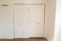 Closed pair of white folding sliding doors installed in a wall opening above wooden floor.