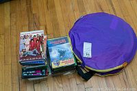 Purple foldable children's tunnel on floor next to stack of DVDs.