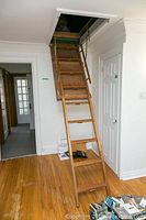 Foldable wooden attic stairs extended from ceiling hatch, showing full length and surrounding ceiling area.