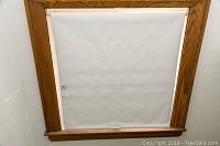 Vinyl roller blind installed in wood-framed window, viewed fully down with minor wear at bottom edge.