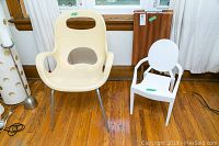 Cream Umbra chair and white child's replica Louis Ghost Chair, set on hardwood floor with wood panel behind
