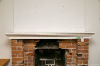 Front view of the painted wood fireplace mantle mounted above brick fireplace, showing dimensions and condition