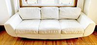 Front view of cream vinyl sofa with three cushions and two pillows, showing overall condition and design, highlighting wear on cushions.