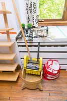 Shows mop bucket with wooden-handled mop, yellow commercial bucket, plastic red bucket, wooden washboard, and a wooden shelf unit
