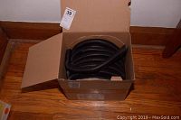 Open cardboard box containing a coiled black flexible corrugated tubing, showing the lot contents clearly.