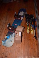 Photo showing two sets of children's skis, one pair with boots, and a Mountain 162 snowboard with bindings. Small cardboard box visible.