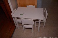 White kids table and four matching chairs set arranged on floor, side angle view showing table and three chairs around it.