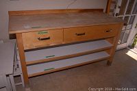 Full view of kitchen island showing solid wood top, three drawers with metal handles, and two white shelves.