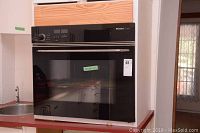 Front view of Miele Classic built-in oven with black glass door and stainless steel handle installed in kitchen cabinetry.