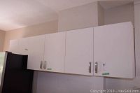 View of the front of the white upper kitchen cabinets mounted on the wall with silver handles, closed doors.