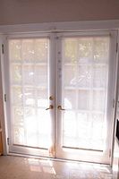 Full view of two cream/off-white roller shades installed on double French door, translucent fabric panel showing through light from outside.