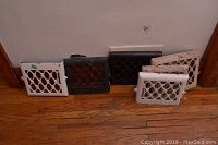 Six metal vent covers of varying colors and paint conditions arranged against a wall on a wood floor.