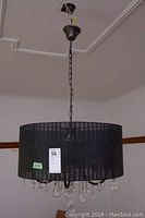 Photo showing the black fabric drum shade chandelier hanging from the ceiling with visible crystal pendants and chain mount.