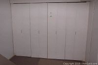 Full view of two adjacent white folding closet doors installed in a residential setting, showing four panels on each door set.