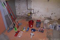 Photo showing various cleaning tools including mops, mop heads, buckets, dustpan, and cleaning agents arranged on an orange floor against a wall.