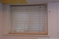 First set of white faux wood horizontal blinds installed in a window, showing tilt wand and lift cord.
