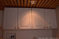 Front view of white upper kitchen cabinets installed on wall, showing four door fronts with rounded raised panel design and round metal knobs.