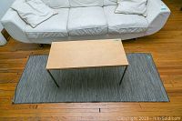 Rug with coffee table placed on top, showing the full rug with a subtle black and white pattern and wear on wood floor.