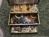 Top drawer view showing assorted bracelets, rings, brooches, and faux pearl necklaces with heart pendants.