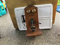 Front view of antique wooden wall-mounted telephone showing brass bells and mouthpiece.