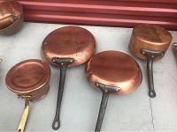 Four vintage copper pans displayed with different handle types and sizes, showing aged patina and wear.