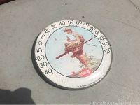 Front view of Coca-Cola Norman Rockwell thermometer outdoors showing temperature scale and artwork.