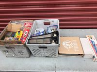 Overview of multiple boxes and binders containing baseball cards and card sets placed outside in front of a red metal door.