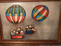 Full view of the framed painting depicting musicians in two hot air balloons with colorful panels against a textured gray background.