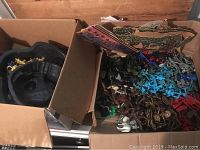 Open cardboard box with black plastic playset pieces and assorted small figures mixed by color.