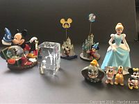 Disney-themed collection with Mickey Mouse snow globe, crystal ballerina block, miniature castles, and various Disney character figurines.