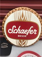 Large bottle-cap shaped Schaefer Beer wall sign close-up with Jack Daniels hat partially visible