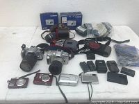 View of entire lot showing cameras, lenses, accessories on white table.