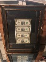 Full frontal view of entire wooden framed uncut bills sheet with black backing and glass.