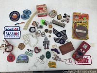 Top-down photo of all items including pins, a toy car, jewelry, cassette tape and badges scattered on a white surface
