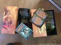 Two boxes of Magic The Gathering cards shown, one with booster pack and cards inside, the other filled with assorted cards.