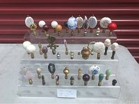 Full display of all 41 lamp finials shown on clear tiered acrylic stand, variety of materials and patterns visible