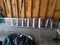 Whole view showing the aluminium ladders lying horizontally against a wall inside a shed.