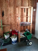 Photo showing grass seed spreader, bags of soil and mulch, buckets, on a wooden shelf in a garage or garden shed