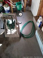 Left side view of plastic hose caddy holding a green garden hose, with a second green hose next to it on the floor.