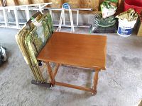 Photo of solid wood end table with four metal TV tables folded and stored on a caddy next to it in a garage setting.