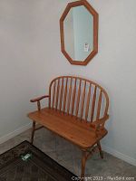 Solid wood hall bench with spindle backrest, armrests, and turned legs placed against a wall with a rug in front.