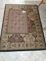 Two stacked rugs on tiled floor showing a floral border larger rug under a smaller geometric pattern door mat.