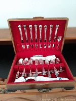Full view of the open wooden canteen showing organized slots holding multiple pieces of silver plated cutlery with ornate floral handles