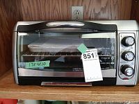Front view of the Hamilton Beach toaster oven with glass door closed, control knobs on the right side, and accessories inside.